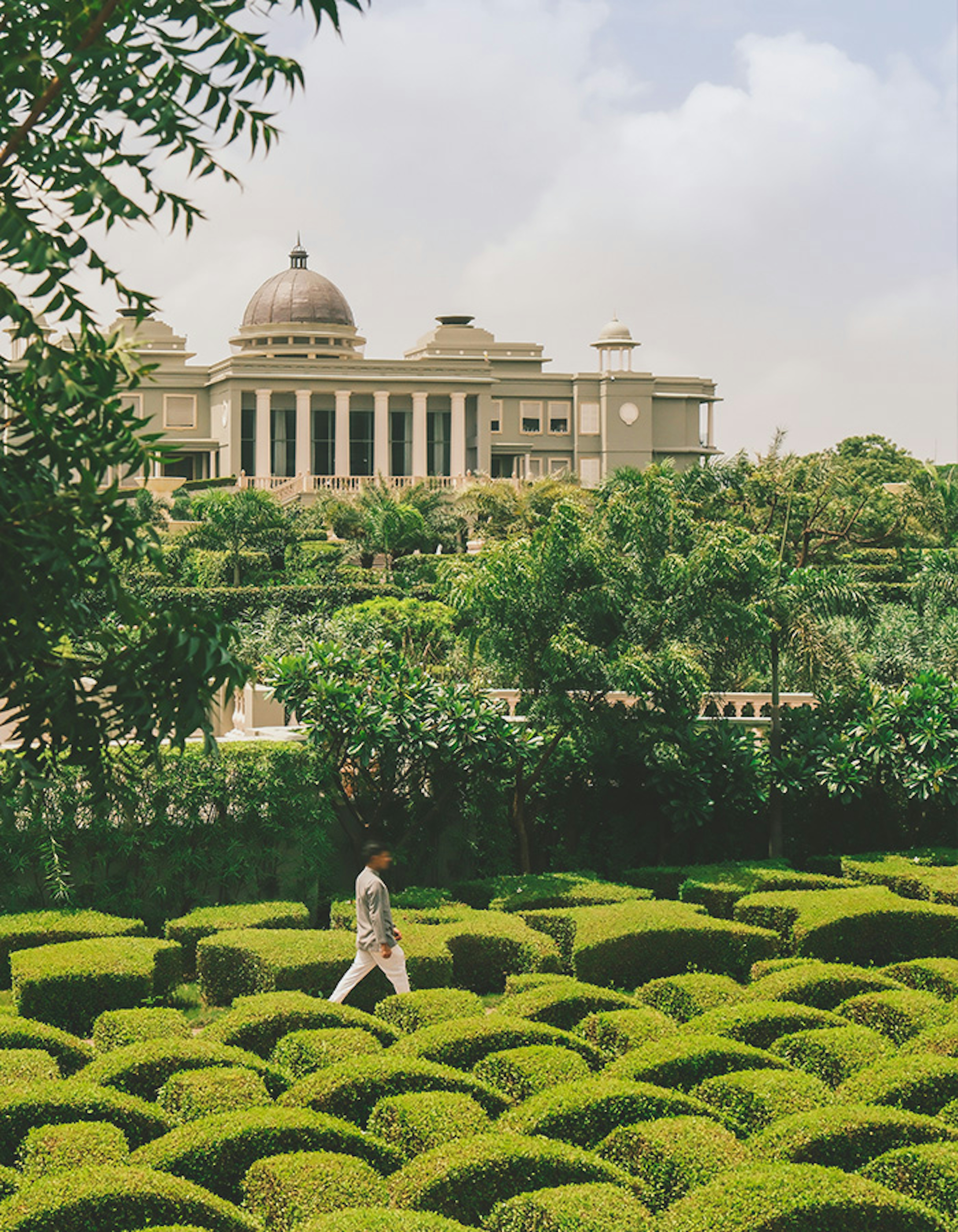 A man strolling through a lush garden in front of the iconic Raffles Hotel.