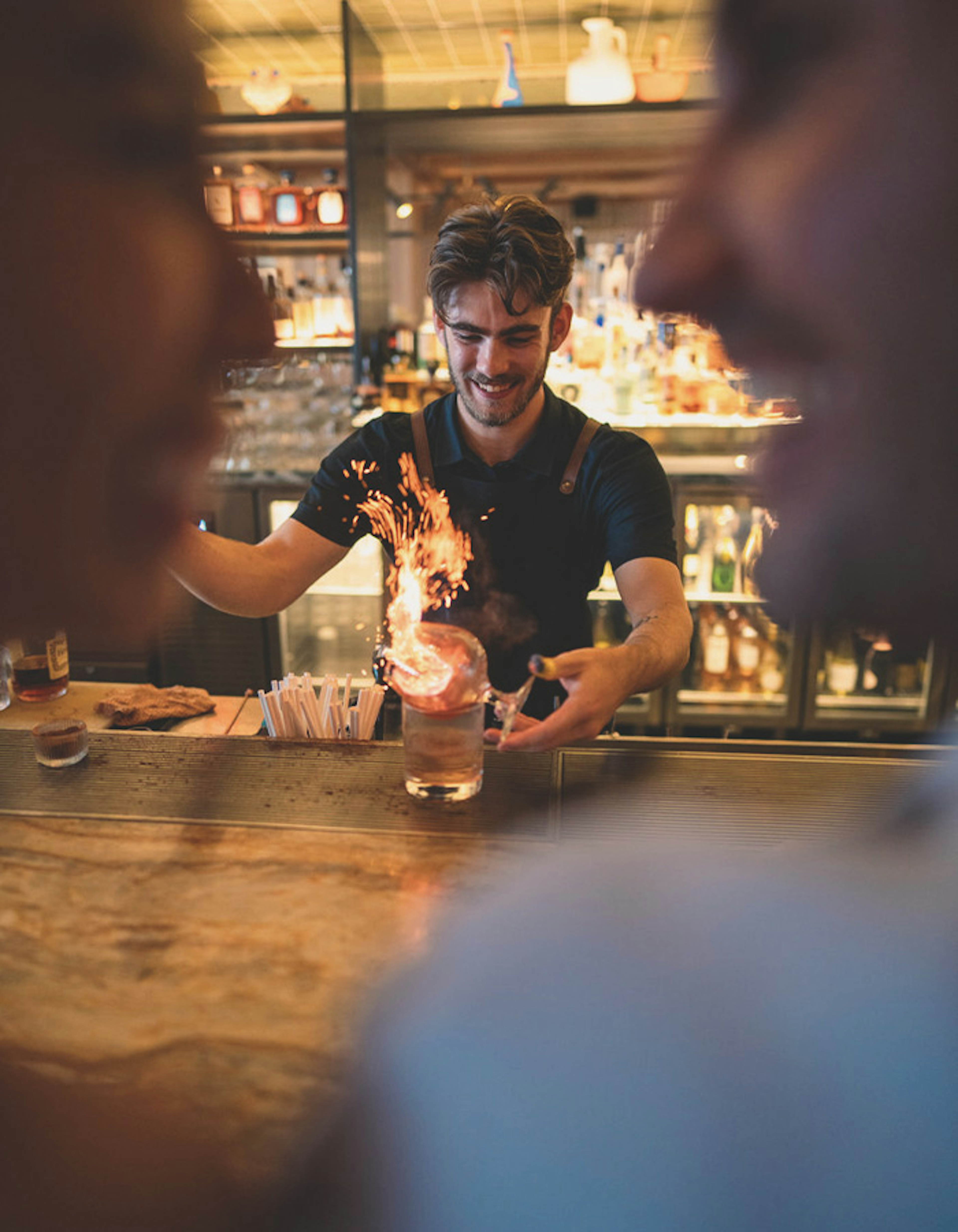 A bartender skillfully preparing a drink in front of two guests seated at the bar.