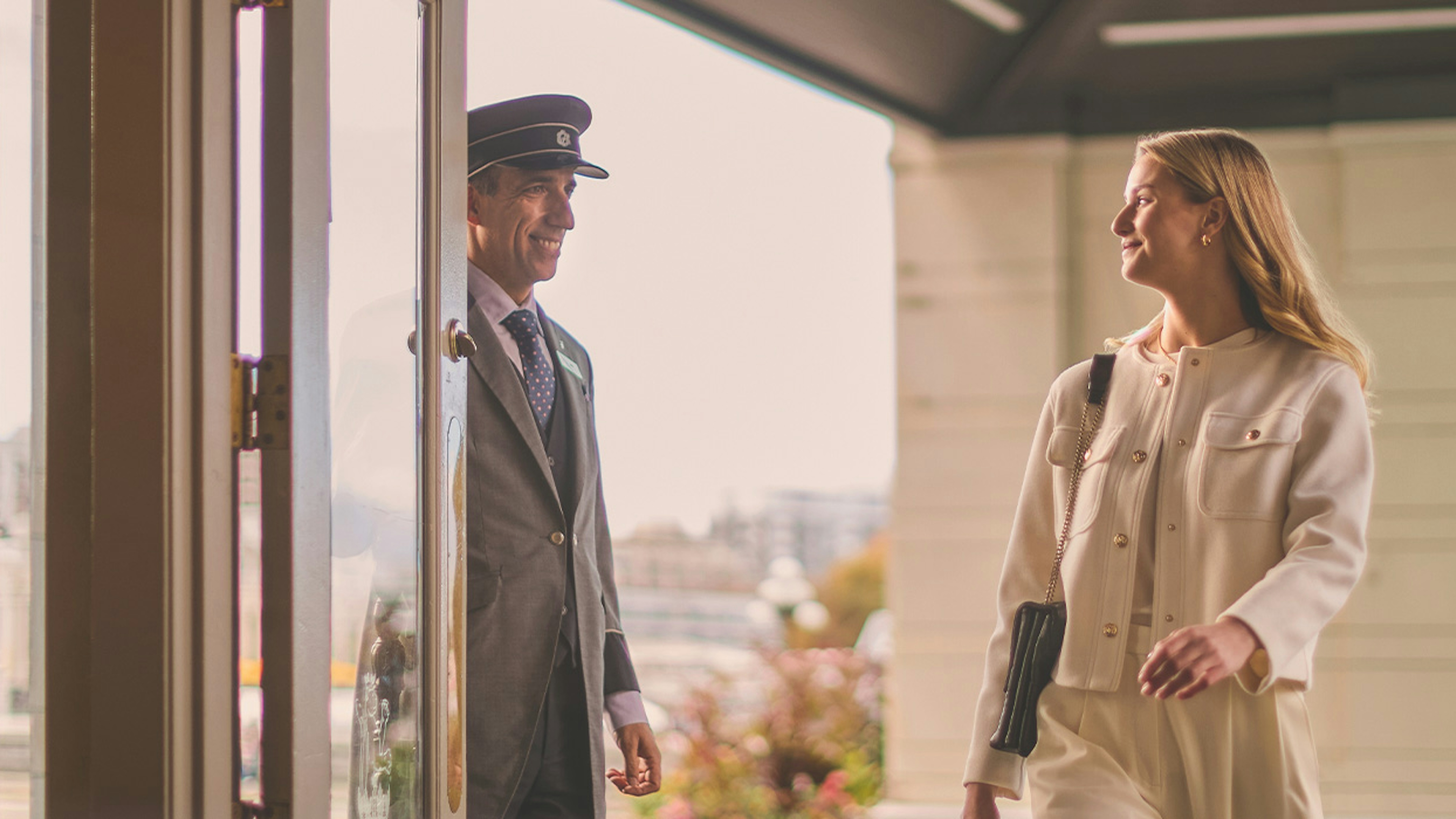 A woman entering a hotel and being warmly welcomed by a doorman at the entrance.