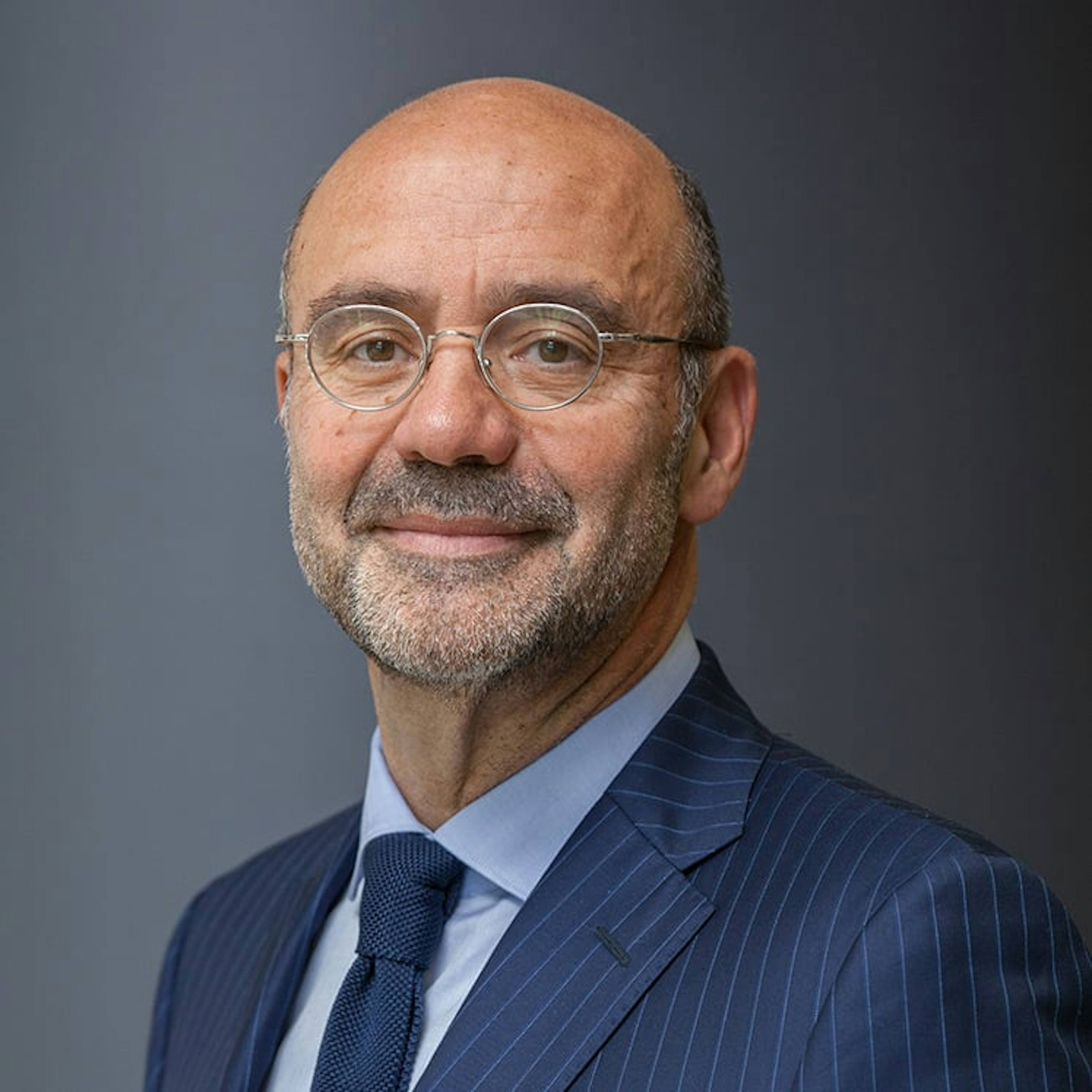 Portrait de Jean-Jacques Morin, un homme barbu aux lunettes rondes, en costume rayé bleu, souriant sur fond gris.