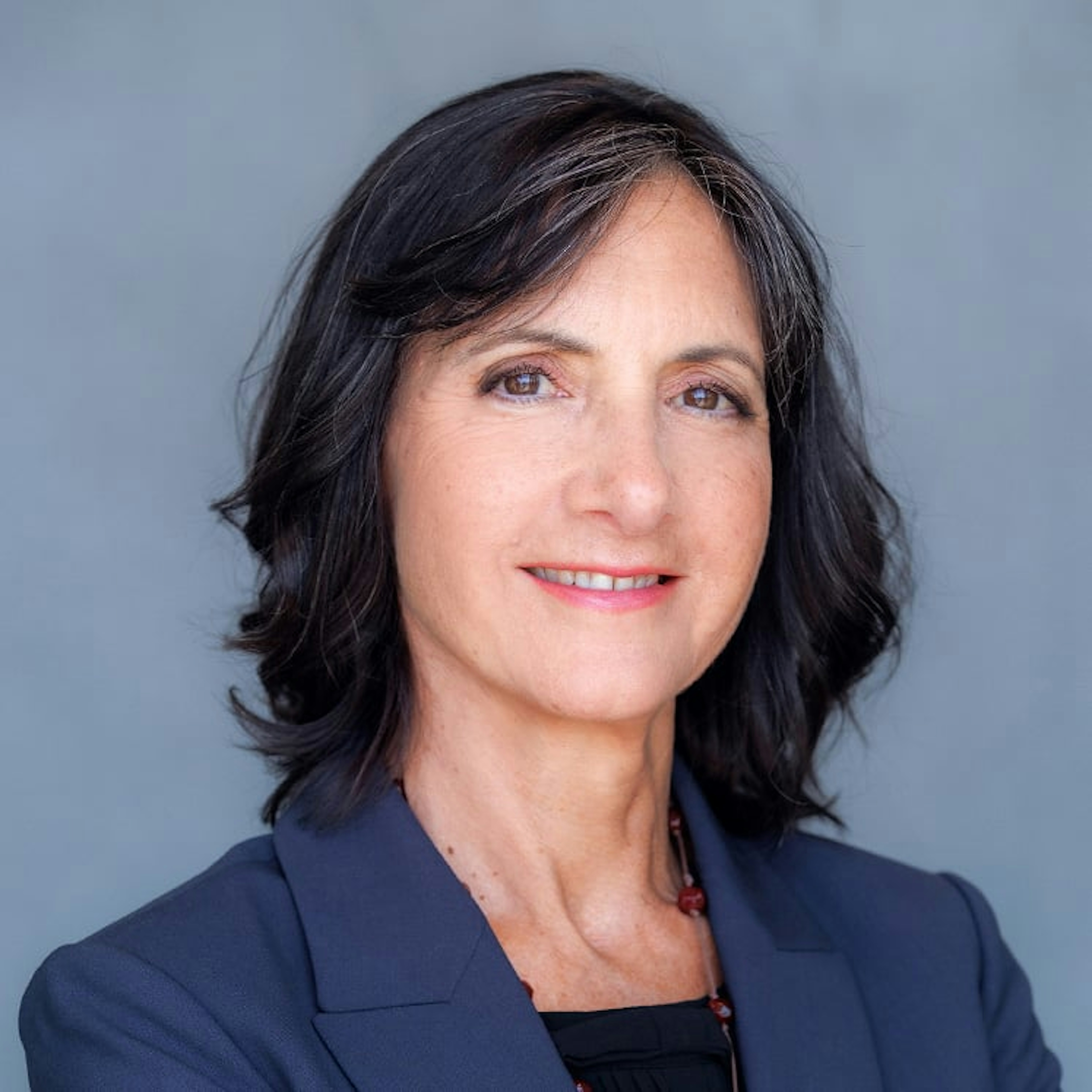 Portrait of Martine Gerow, a woman with short dark hair, wearing a black blazer and a dark top, smiling against a gray background.