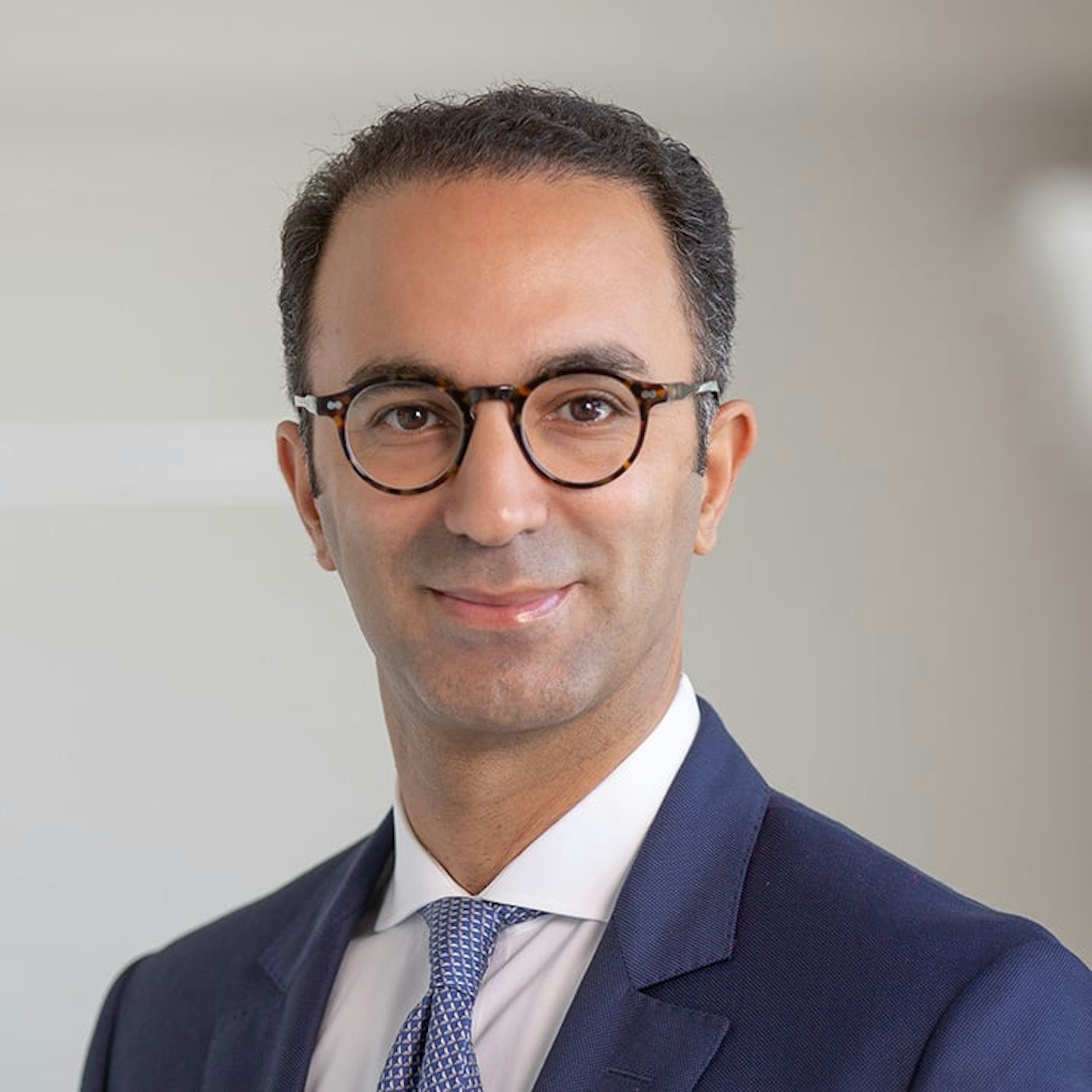 Portrait of Kamal Rhazali, a man with dark hair, round glasses, wearing a blue suit and patterned tie, smiling.